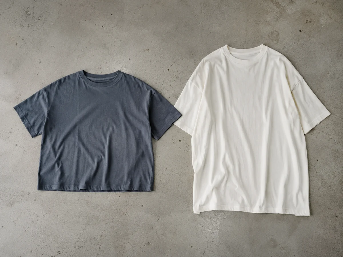 Two plain T-shirts laid flat side by side: one short broad boxy shirt, one longer oversized shirt with dropped shoulder seams. Whole garments visible.