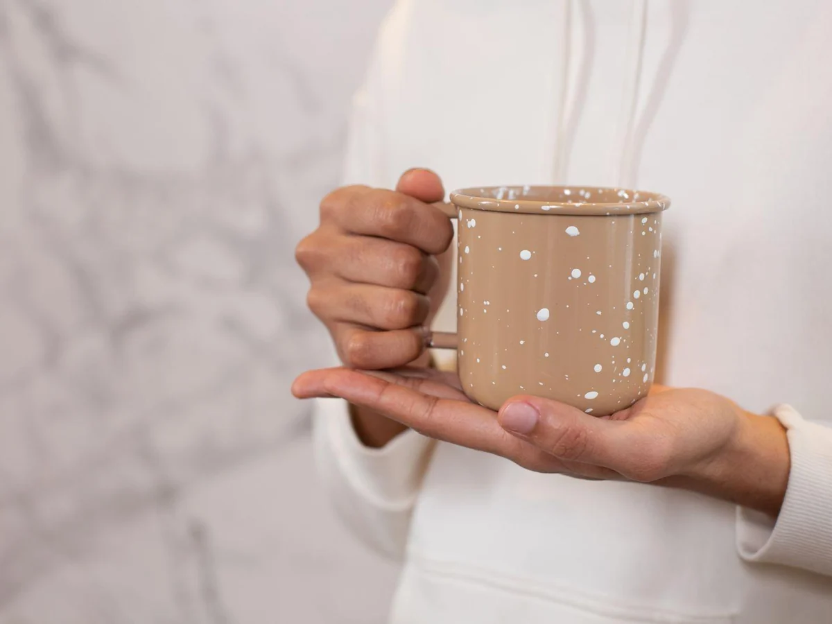 Hands holding a speckled mug by its handle and base.