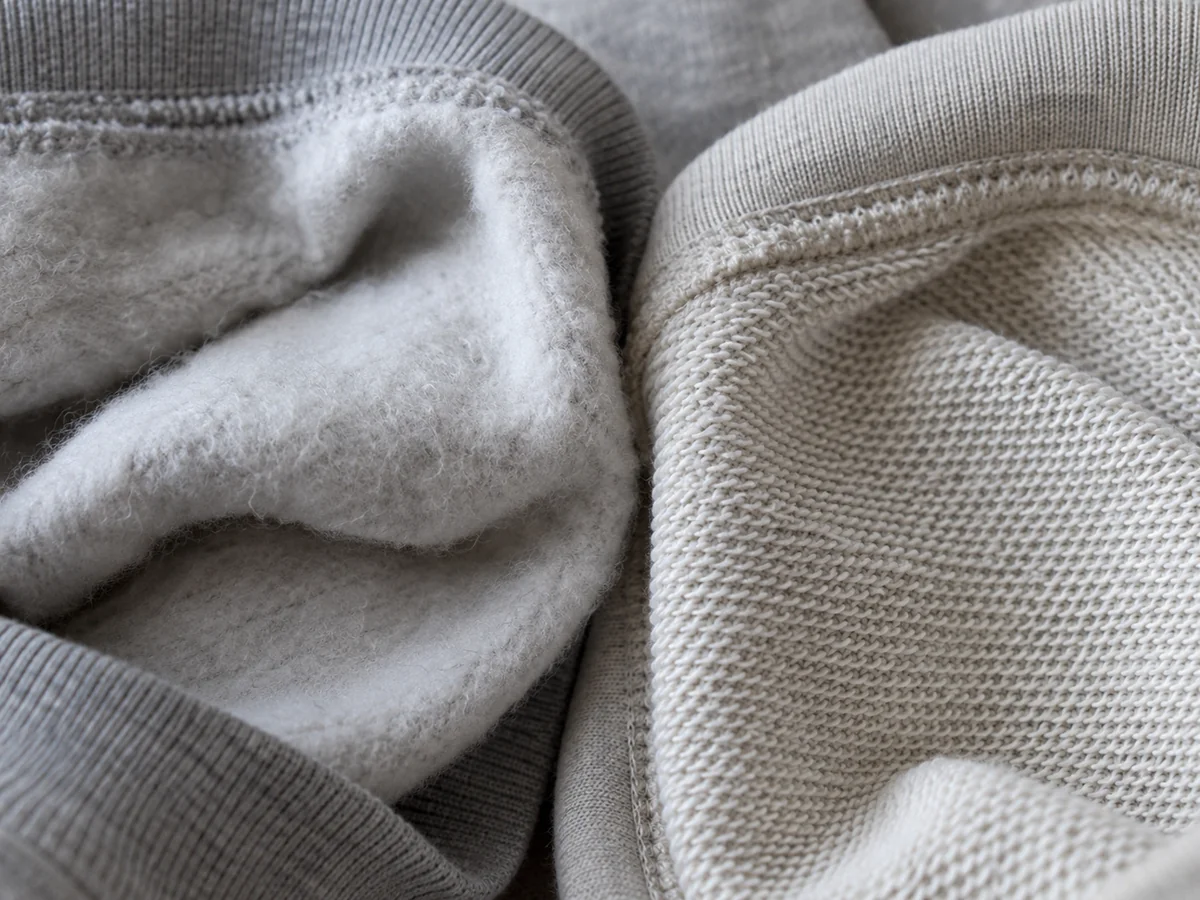 Macro comparison of the inside of two sweatshirt fabrics: fluffy brushed fleece on the left and neat loopback terry loops on the right.