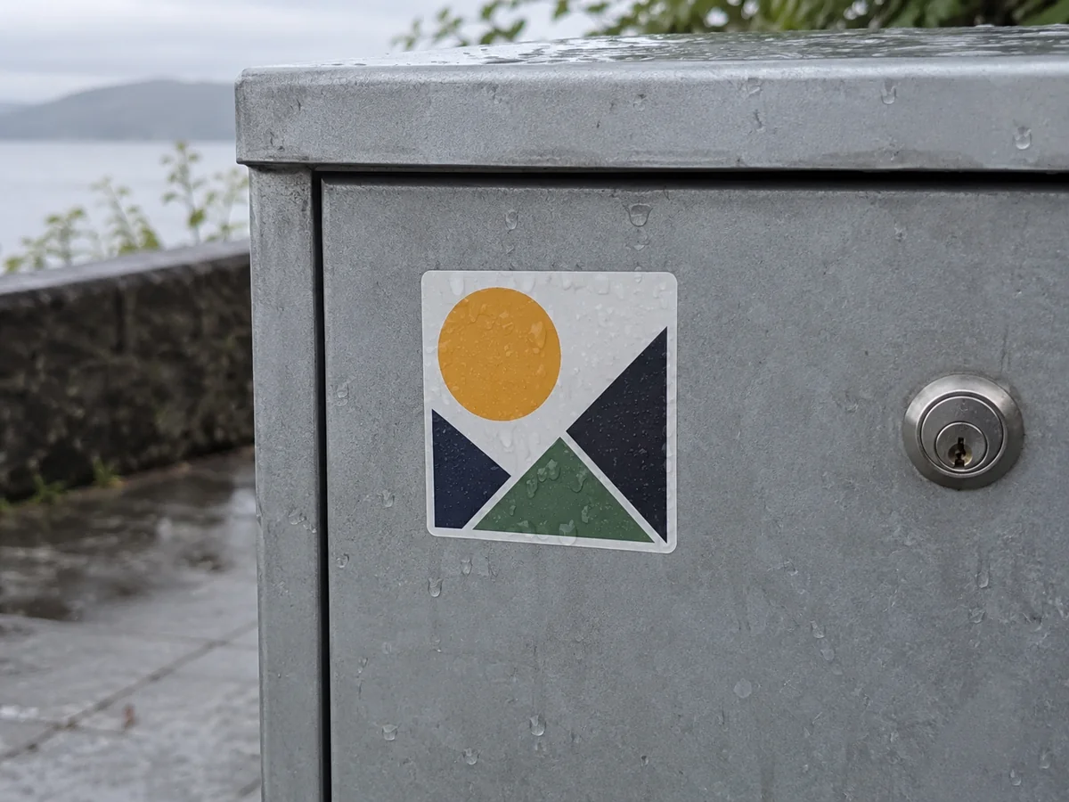 A weather-resistant original geometric sticker on a clean unbranded outdoor metal box with a few raindrops, no peeling or false warranty text.