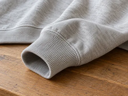 Close-up of a sweatshirt wrist cuff in ribbed cotton with sleeve fabric softly folded beside it, no hands stretching it.