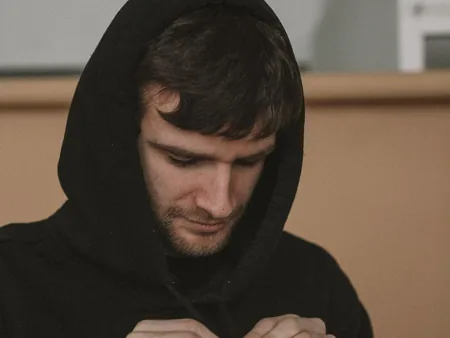 A person wearing a raised black hood and adjusting its drawstrings.