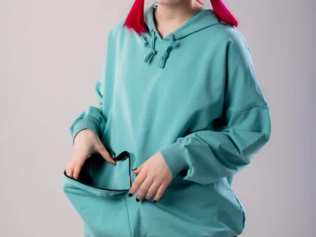 A person pulling open the kangaroo pocket of a teal hoodie.