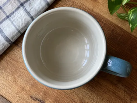 Top-down close-up into an empty glazed ceramic mug, smooth glossy inner surface and light reflected on the glaze.