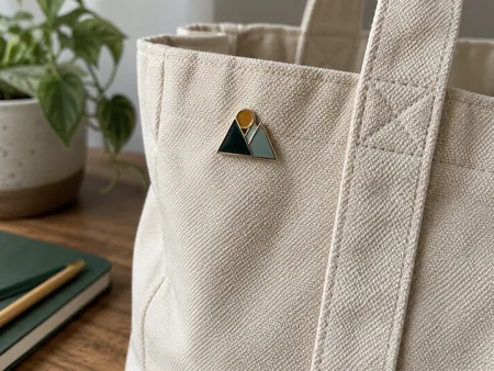 Close-up of a small original geometric enamel pin on the thick canvas panel of a tote, pin attachment area visible, no recognised art.