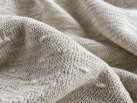 Extreme close-up of oatmeal slub cotton knit fabric with naturally irregular thicker yarn slubs clearly visible in side light.