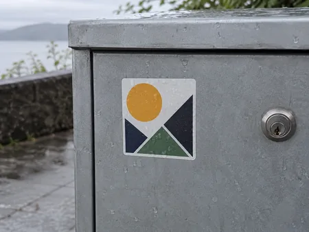A weather-resistant original geometric sticker on a clean unbranded outdoor metal box with a few raindrops, no peeling or false warranty text.