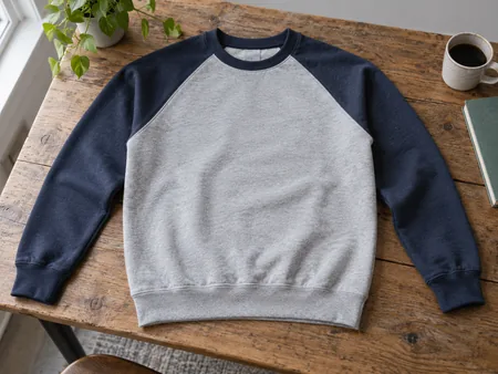 A plain two-tone raglan sweatshirt laid flat, diagonal sleeve seams from neckline to underarm clearly visible.