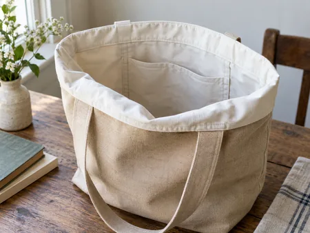 A plain canvas tote held open with a contrasting pale cotton lining folded over the rim, clearly showing inner construction.